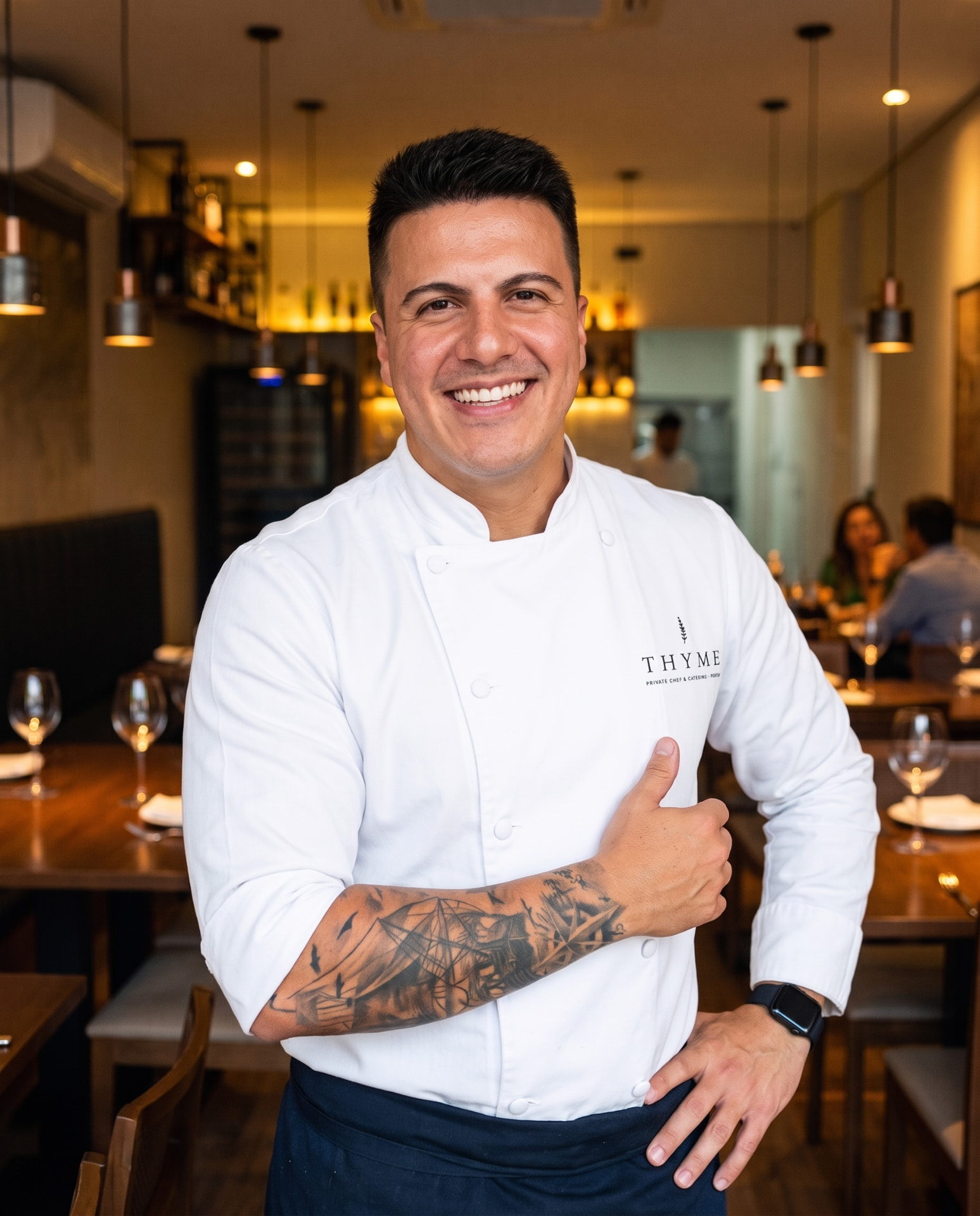 Murilo Lima, chef do Thyme, de jaqueta branca bordada com o nome da marca, num salão de jantar privado
